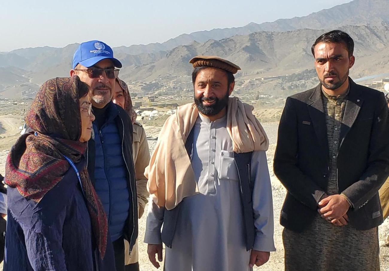 تقف امرأة ترتدي وشاحًا بجانب رجلين يرتديان قبعات ورجل يرتدي سترة.