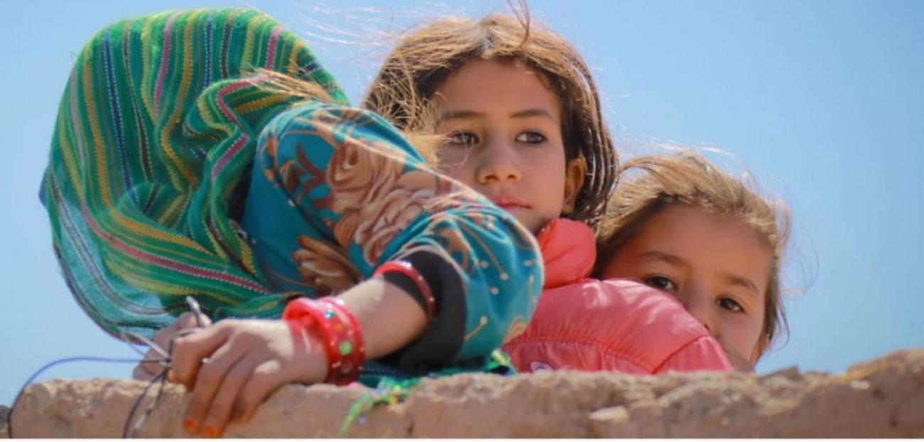 Three Afghan girls in blue dress, pink dress, hidden behind a wall