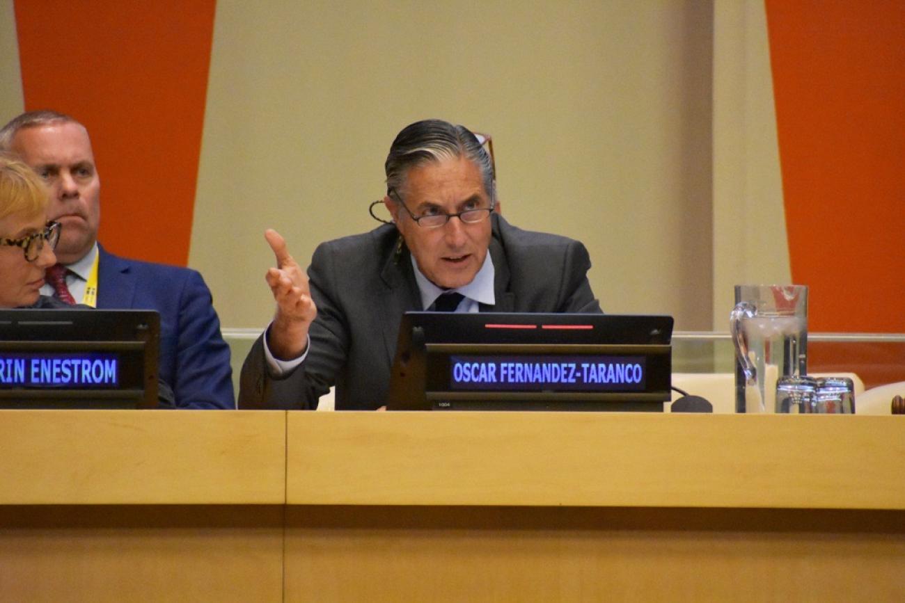 Man in a grey suit sitting at a podium at the united nations 