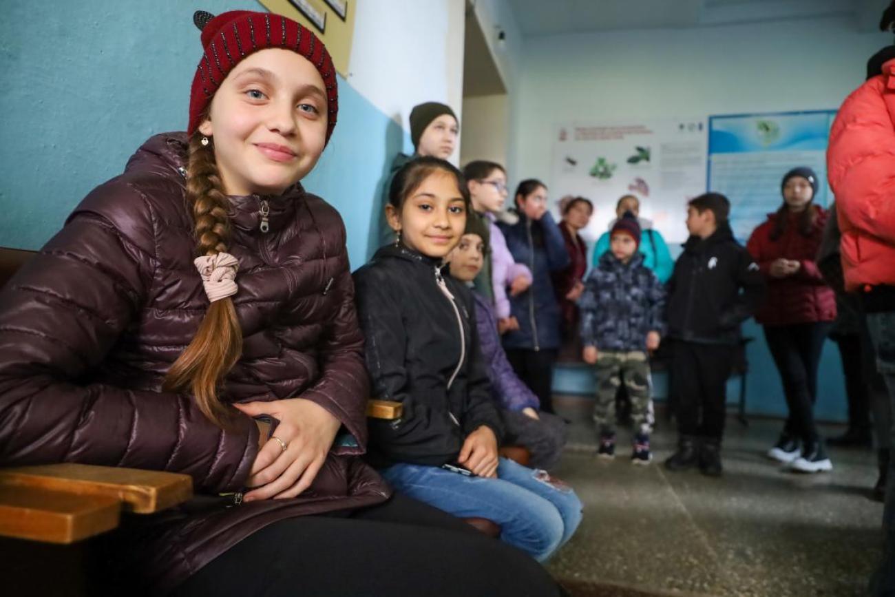 A group of children is jackets and winter clothes stand in a school classroom