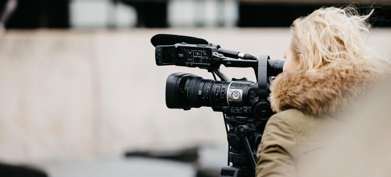 Фотография женщины, блондинки, со спины, которая стоит рядом с видео камерой