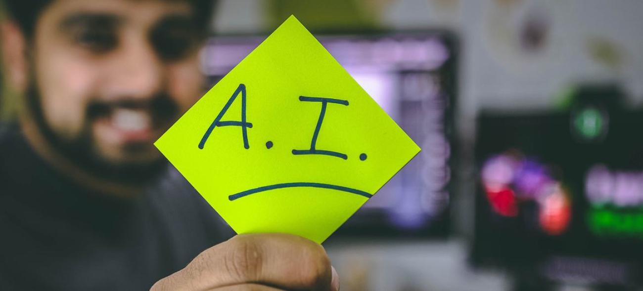 A man with a beard holds up a yellow stickie note, with "A.I" written on it.