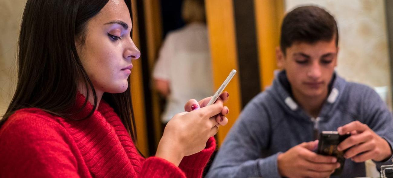 Young people look down and play on their phones.
