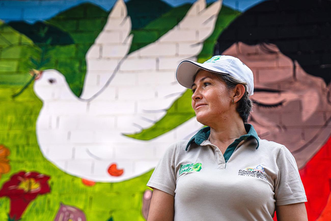 A woman in a grey shirt stands in front a mural with a white dove of peace