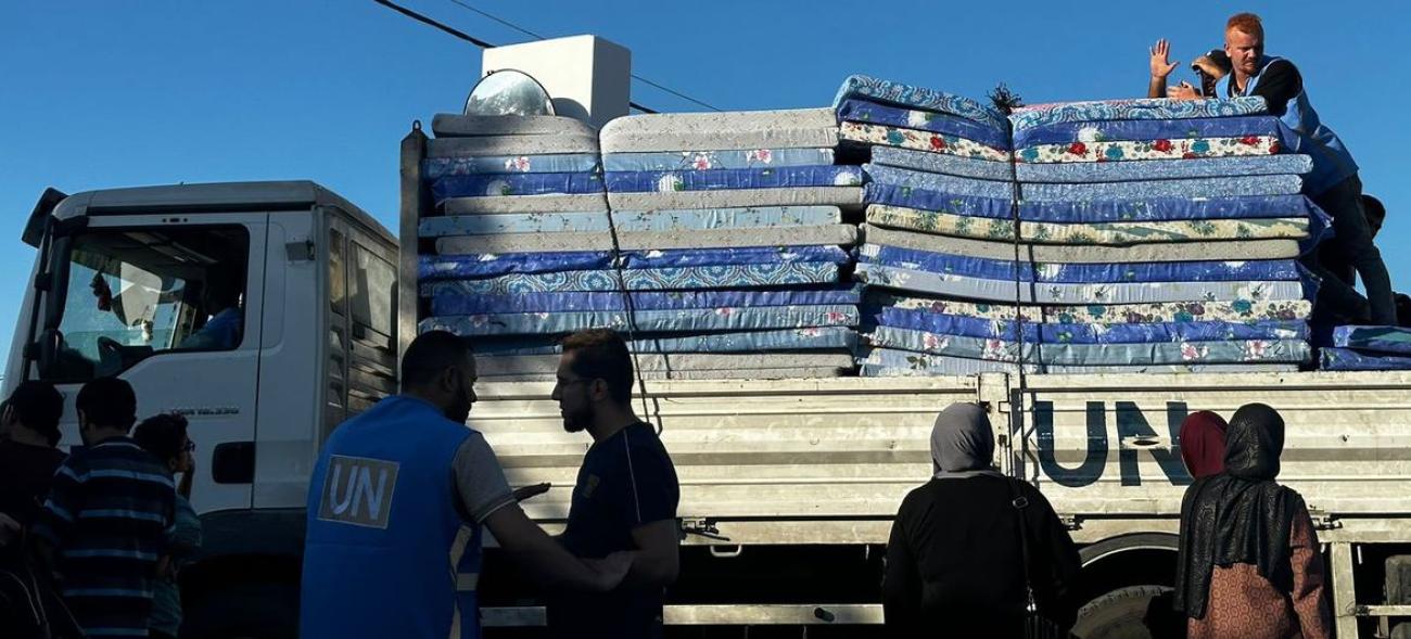 A big UN truck with mattresses stands as people try to unload