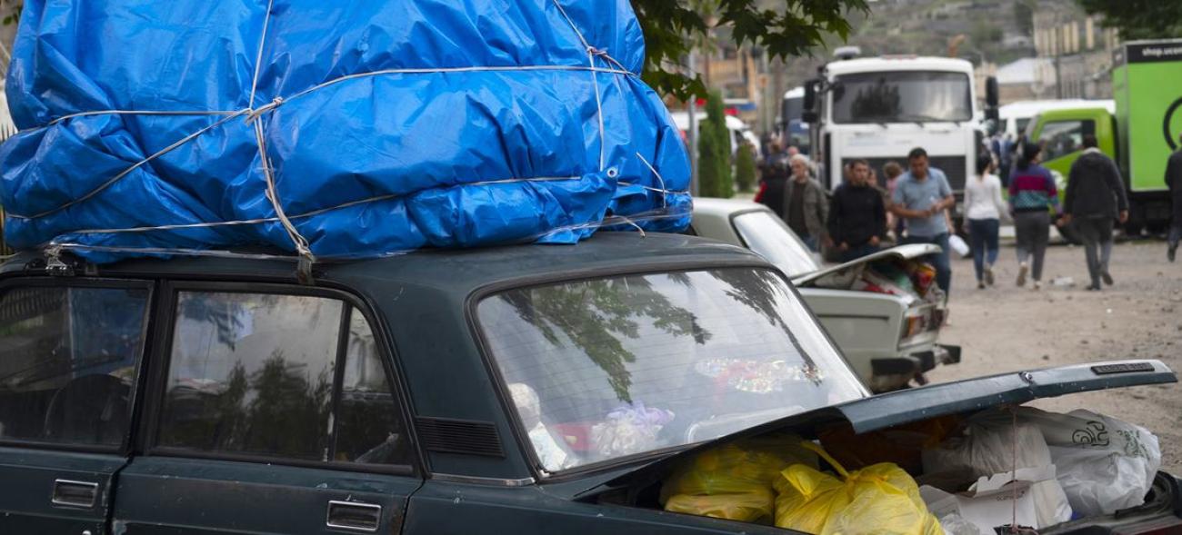 A car with bags loaded in the trunk and a bulky blue tarp on top.