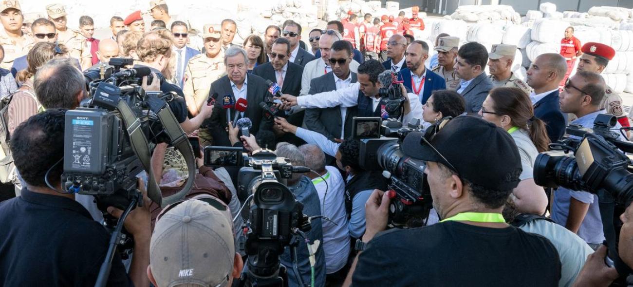 UN officials and security stand around microphones and speak to media and members of the press.