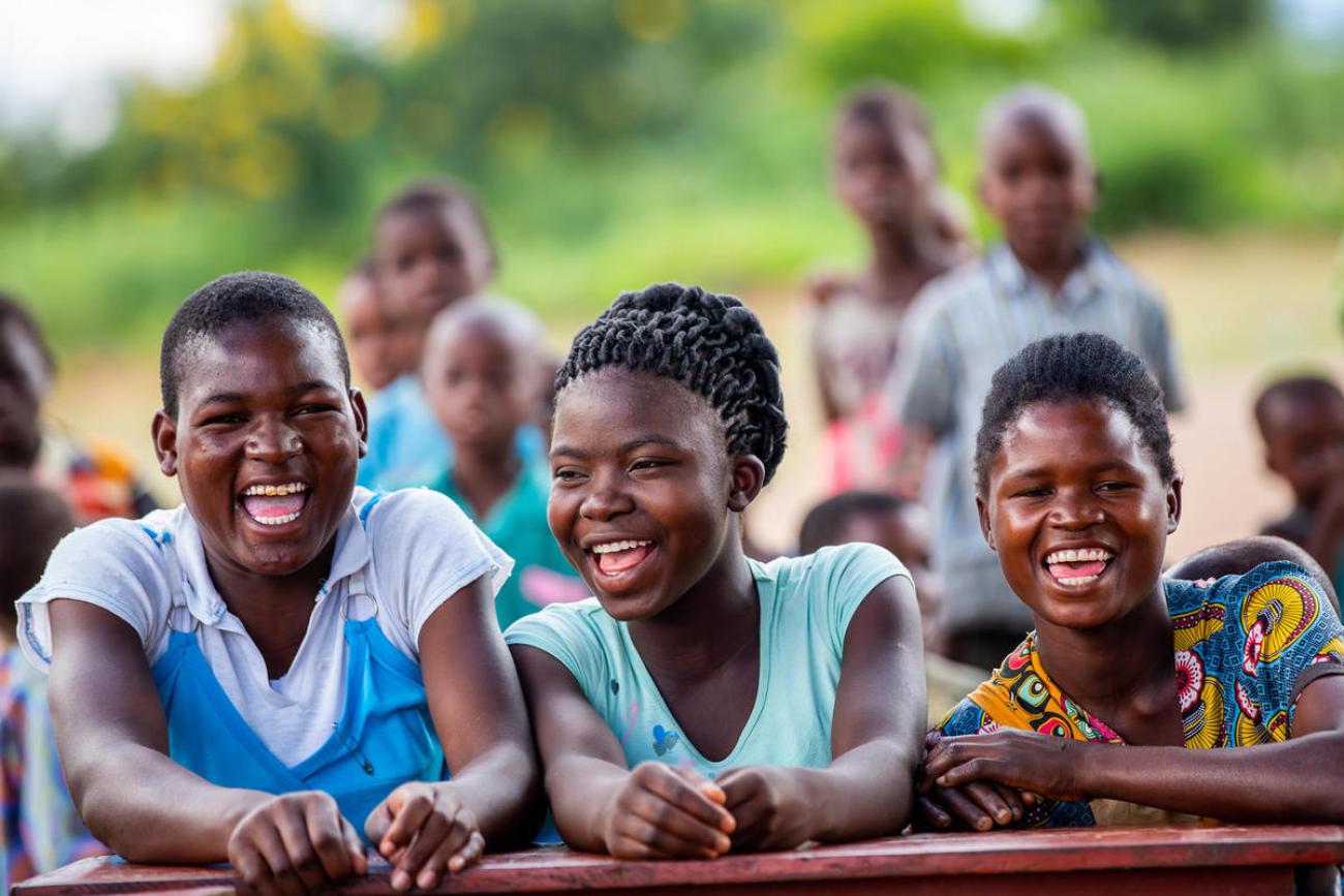 three young people sit next to each other outside laughing towards camera
