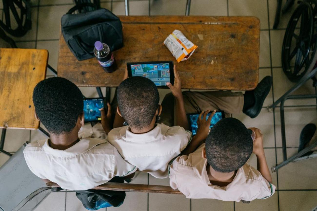 An aerial shot of three children cover over a screen in a school