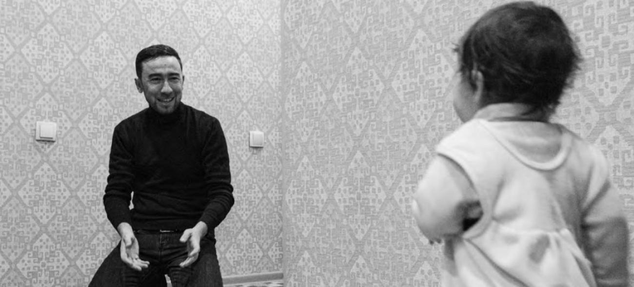 Отец сидит на стуле и с улыбкой общается с маленьким ребенком