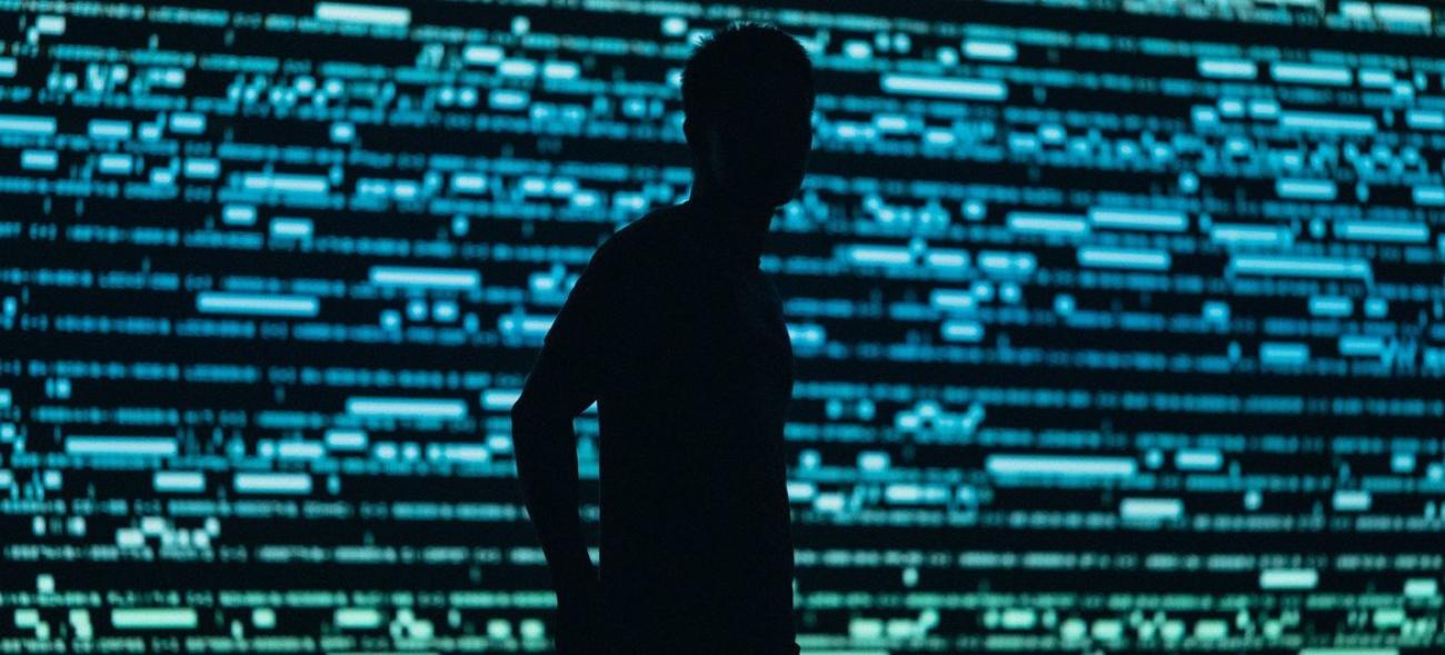 A silhouette of a man against a screen with code written all over it