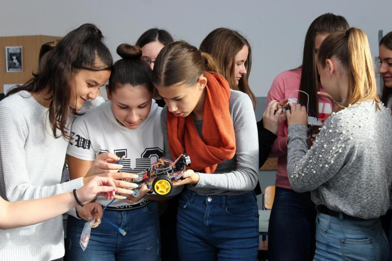 A group of girls huddle around each other as they examine some mechanical parts for a robot.