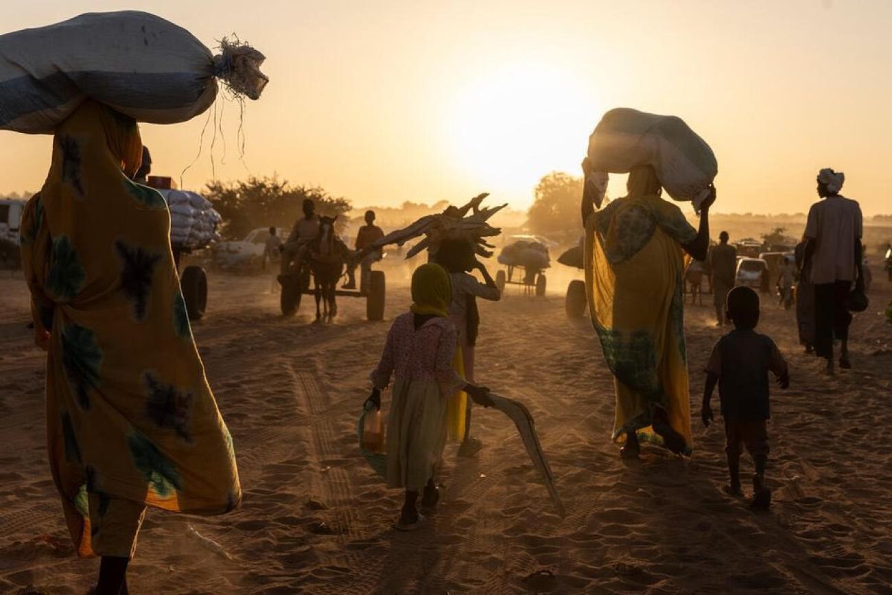 A silhouette image of women, men and children trudging through the sand in Chad with their belongings on their backs and heads.