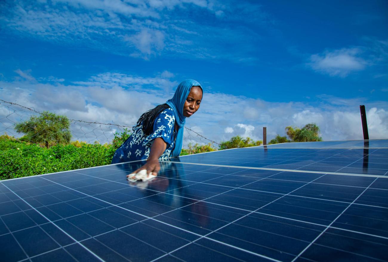 A woman in a blue dress wipes down a solar panel in Africa