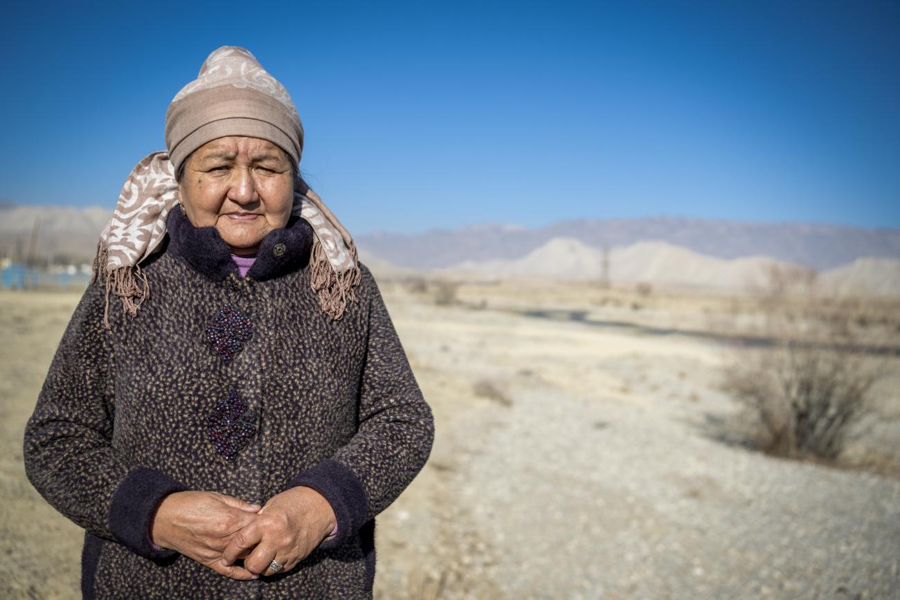 A woman in a thick jacket and a woollen cap stands amid a deserted land