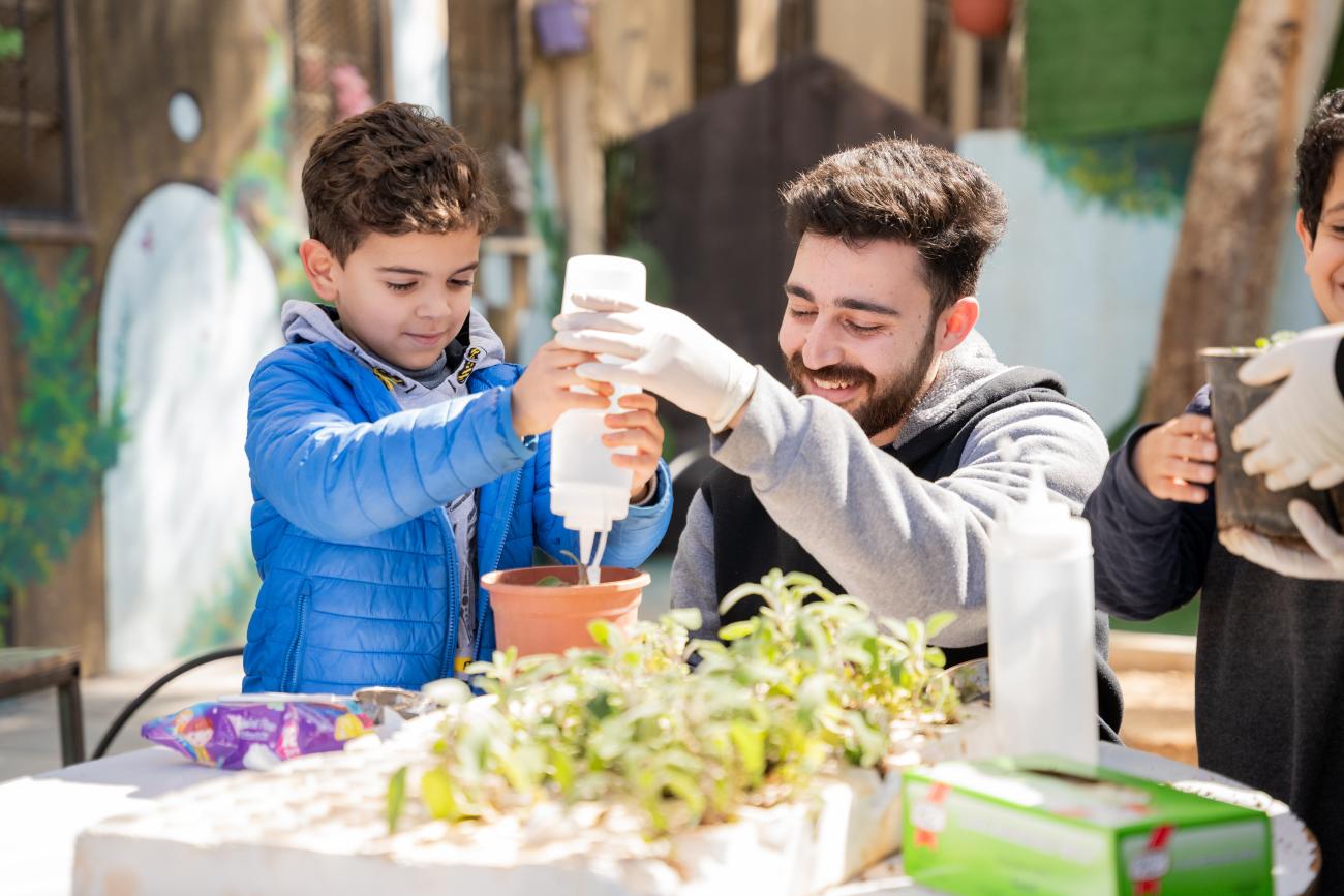 A man and a child hold a bottle of water to water a little plant in a container.