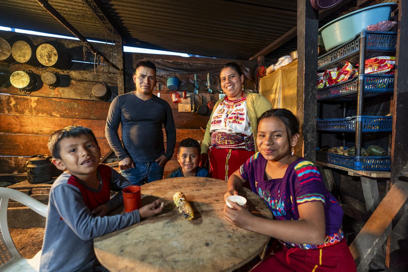 A family sits around a table, they are looking at the camera and smiling