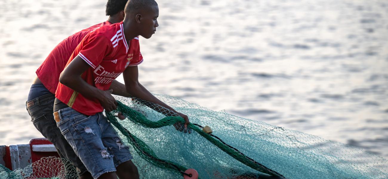 Two young men are on a boat in the water fishing with a net