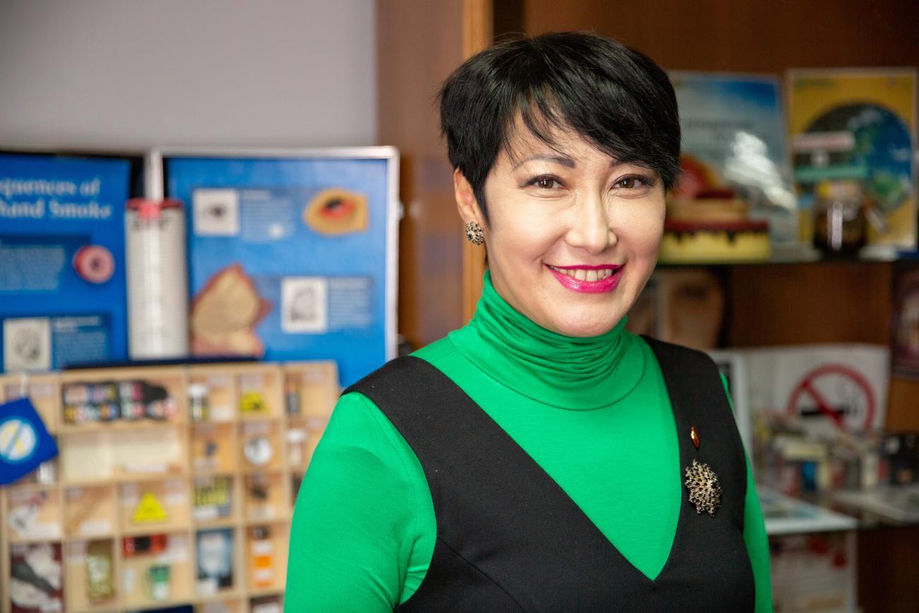 A woman wearing a green top and a blazer looks at the camera and smiles