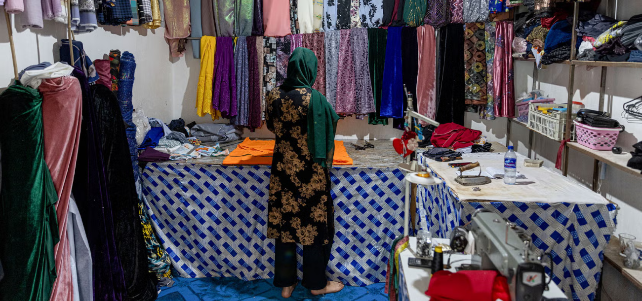 A woman in a dark green dress stands in front of rolls of cloth in a small shop
