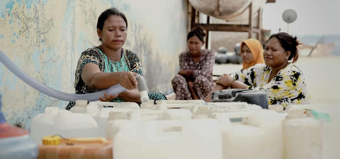 A group of women fill containers with water through pipes