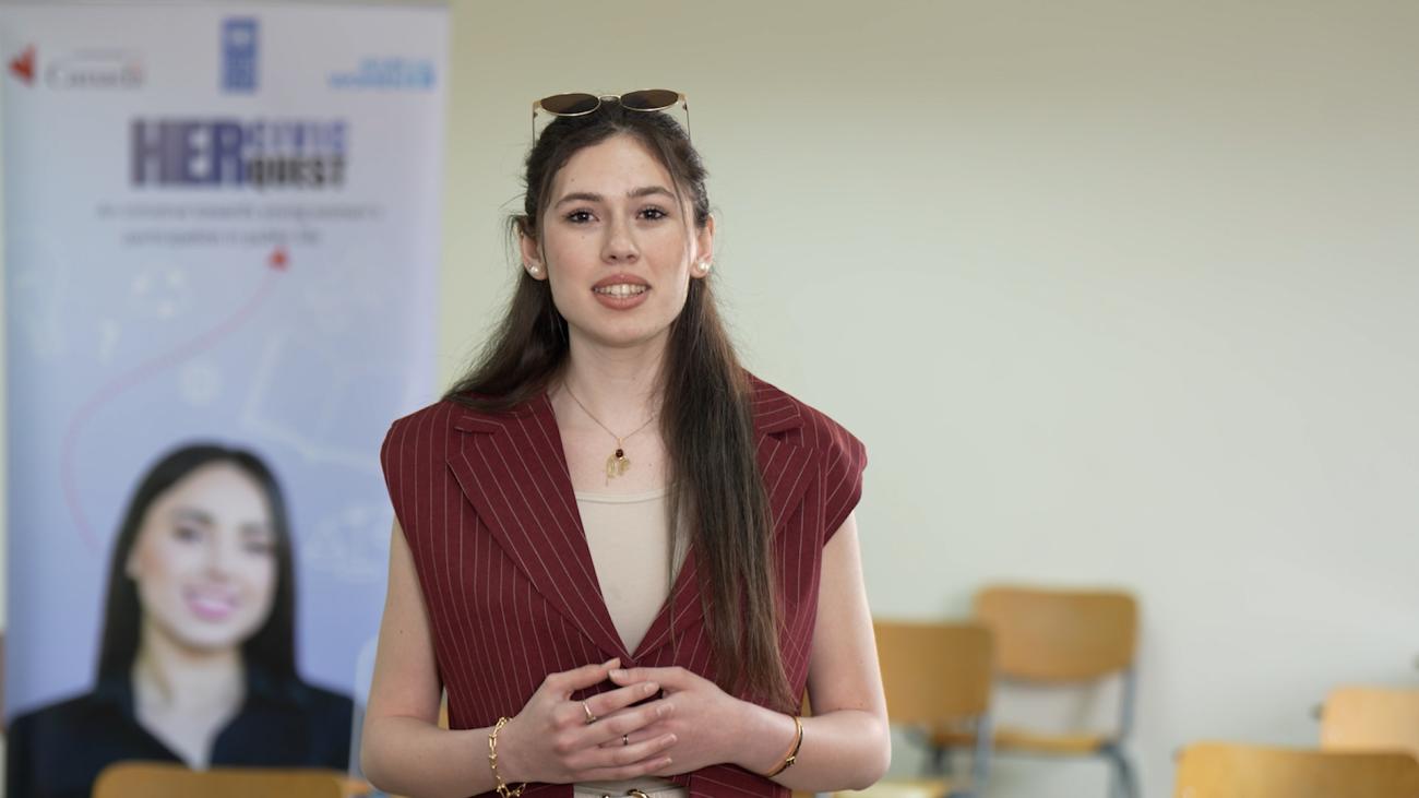 امرأة ترتدي قميصاً خمري اللون تتحدث أمام مجموعة من الأشخاص.