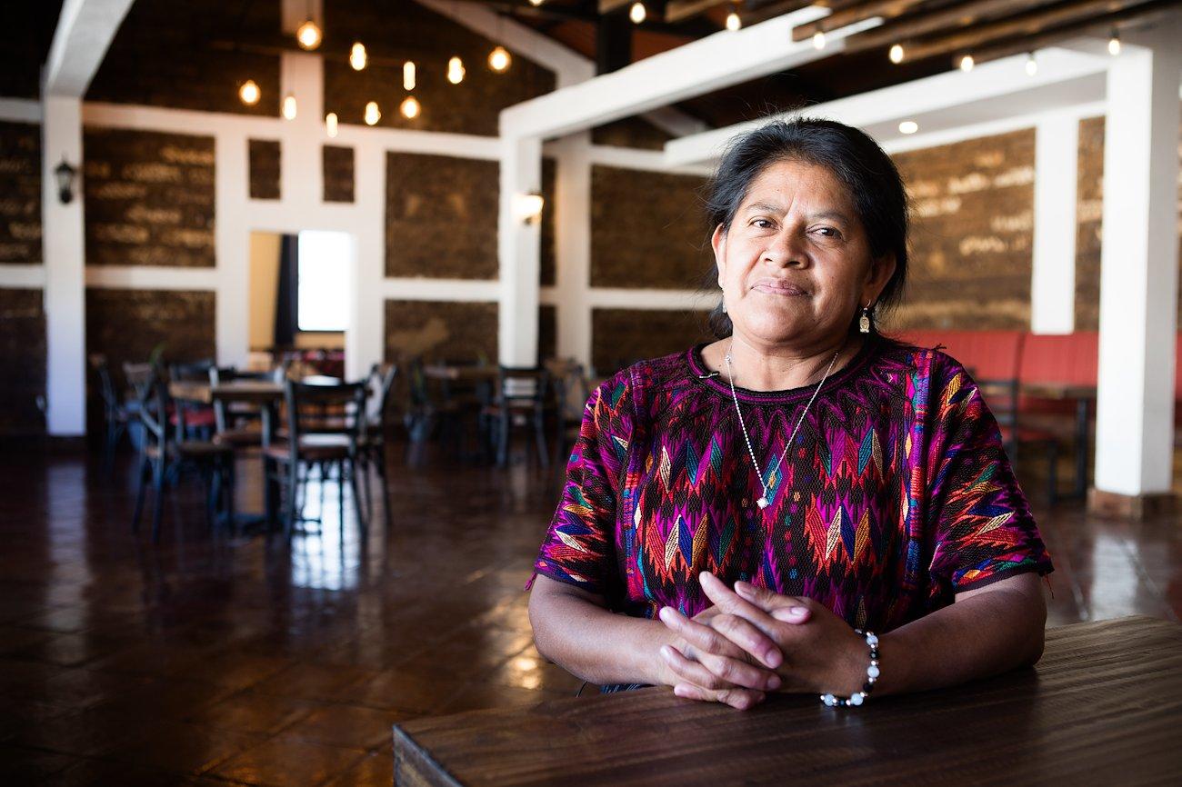 A woman is seated indoors and looking at the camera 