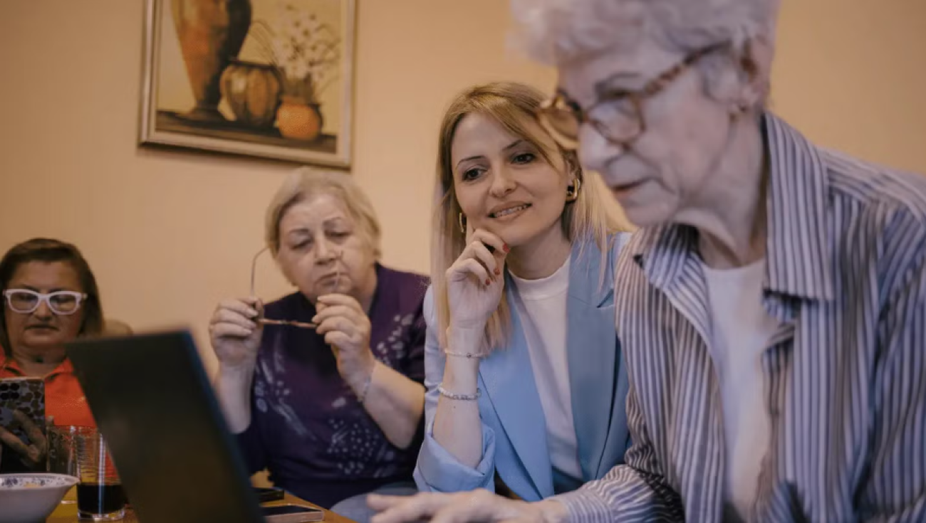 A group of pensioners are gathered around a laptop.