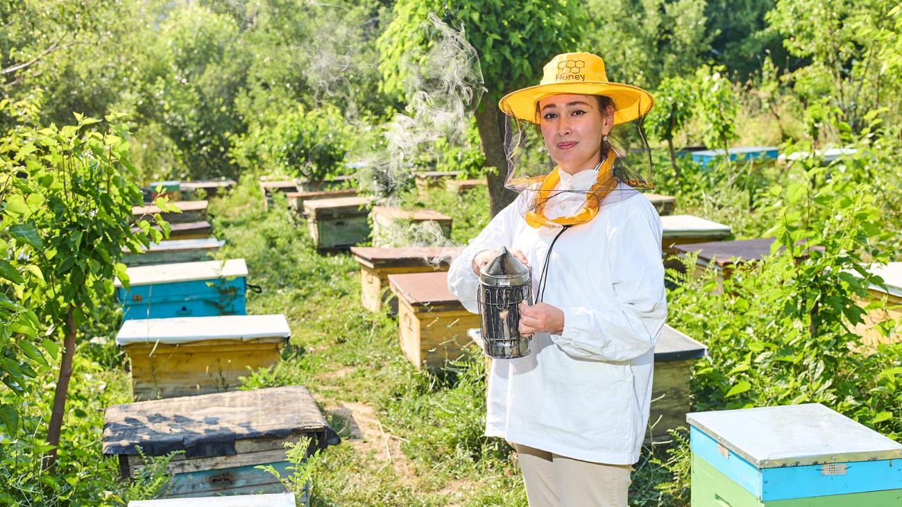 An Uzbek woman beekeeper stands in front of her beekeeping operation.