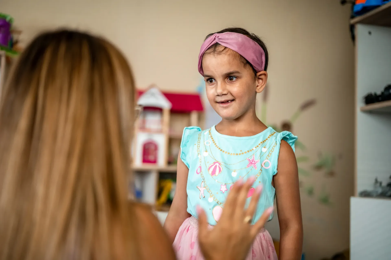 Девочка смотрит на социального работника и улыбается.