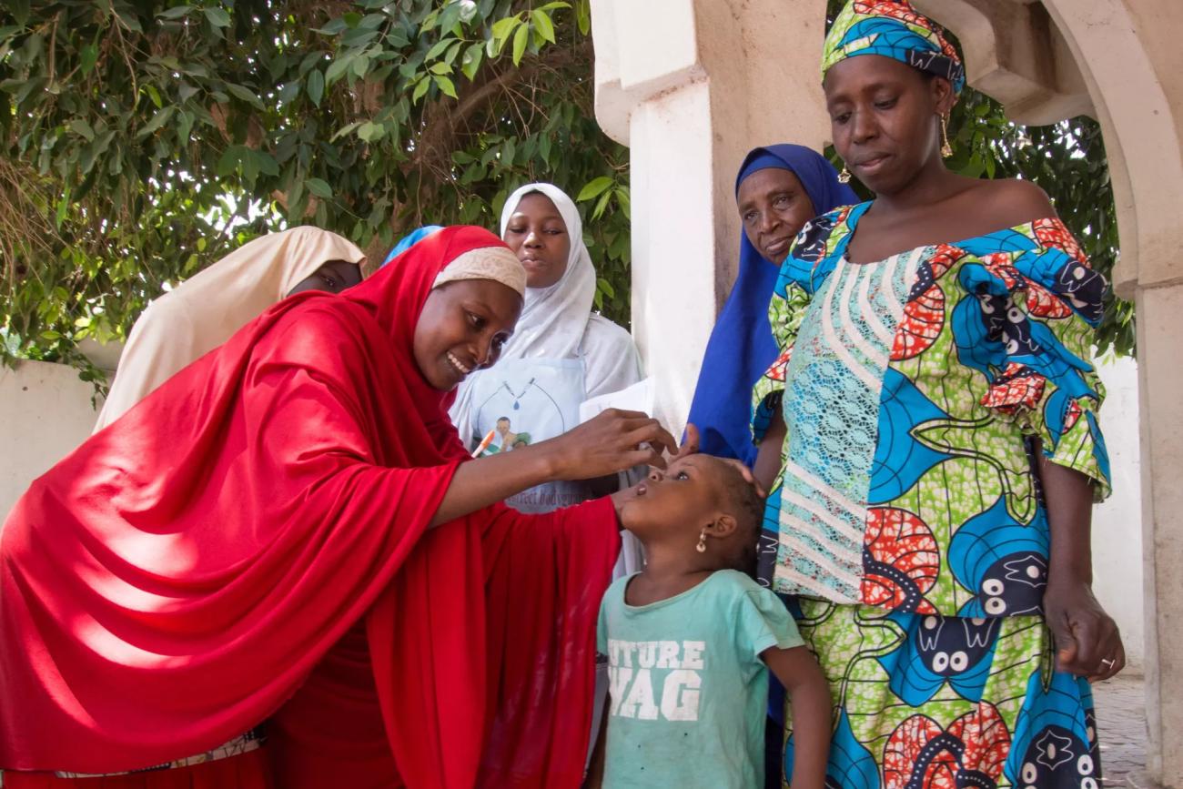 A woman in Nigeria administers a vaccine to a young girl in front of other women.