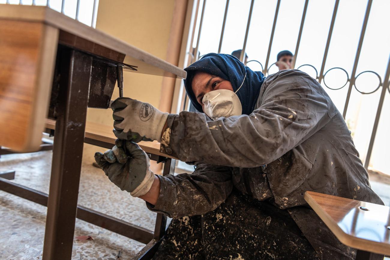 A woman in Iraq fixes a desk in a school.
