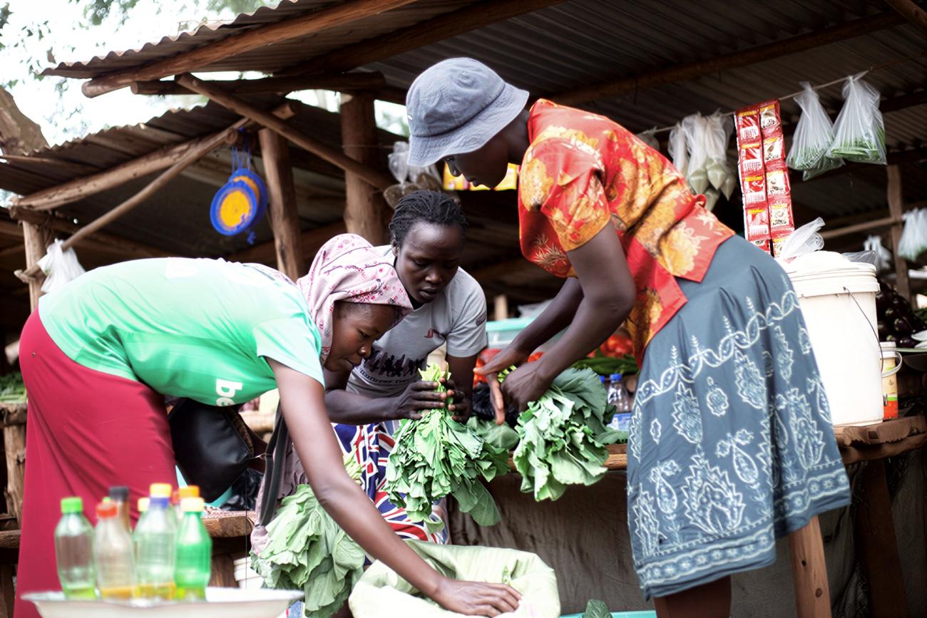 Three women in Uganda sell fresh vegetables as part of their agribusiness.