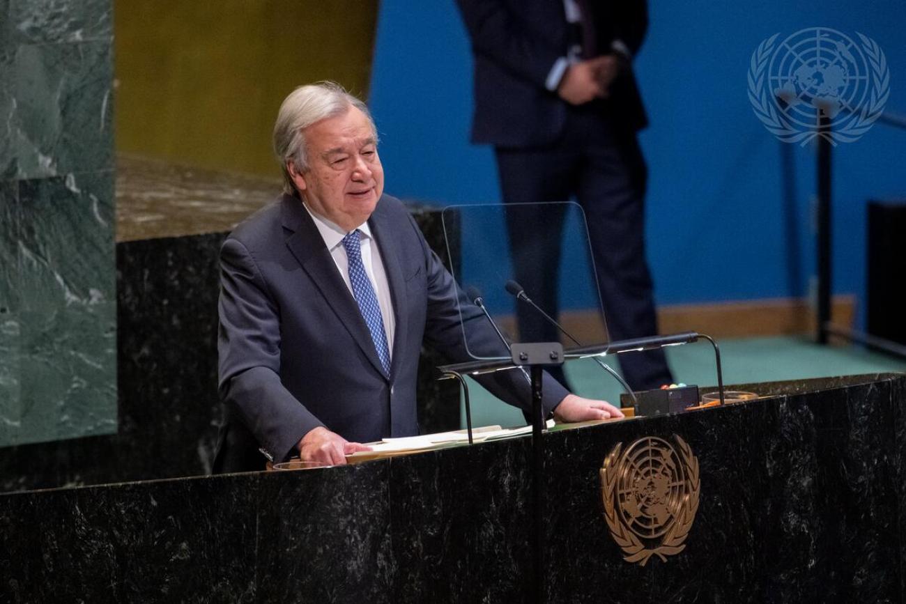 A man inn a dark grey suit and blue tie, the UN Secretary-General, speaks from a podium at the UN building