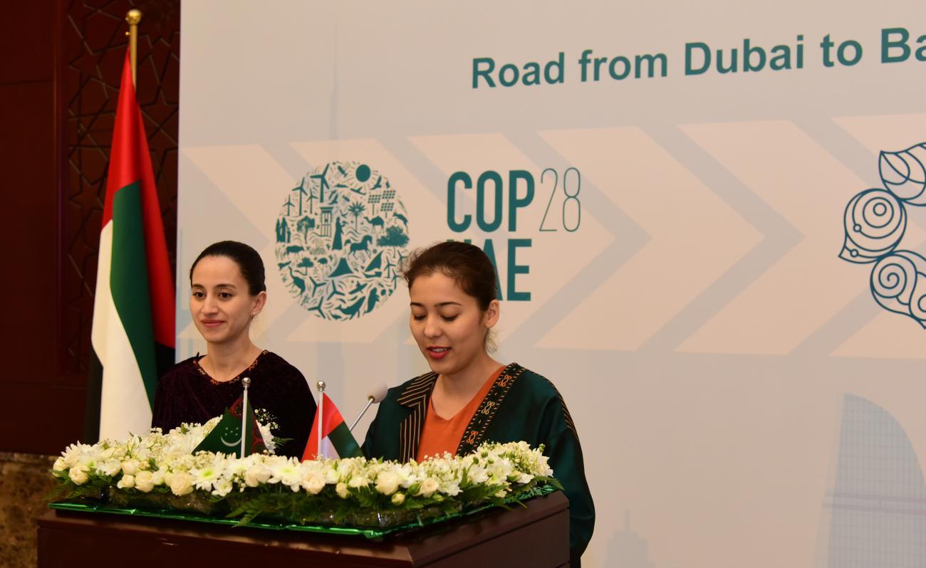 Две девушки выступают с речью за трибуной, украшенной цветами.