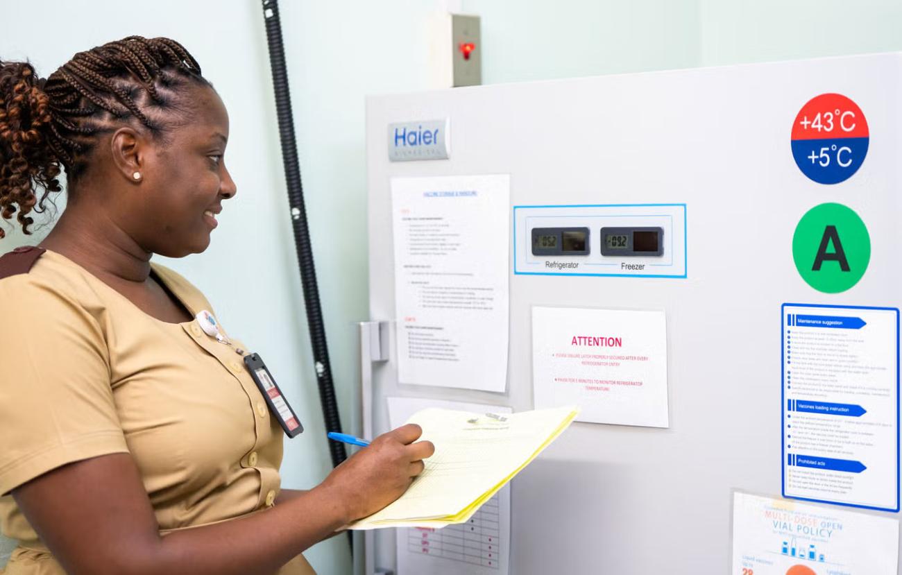 A health worker in Trinidad and Tobago takes notes in front of a vaccine storage refrigerator.