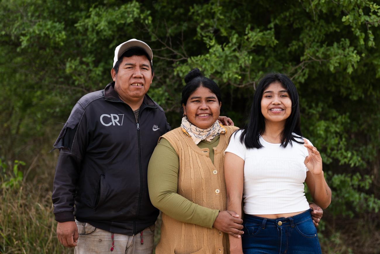 Tres personas sonríen juntas al aire libre frente a unos árboles.
