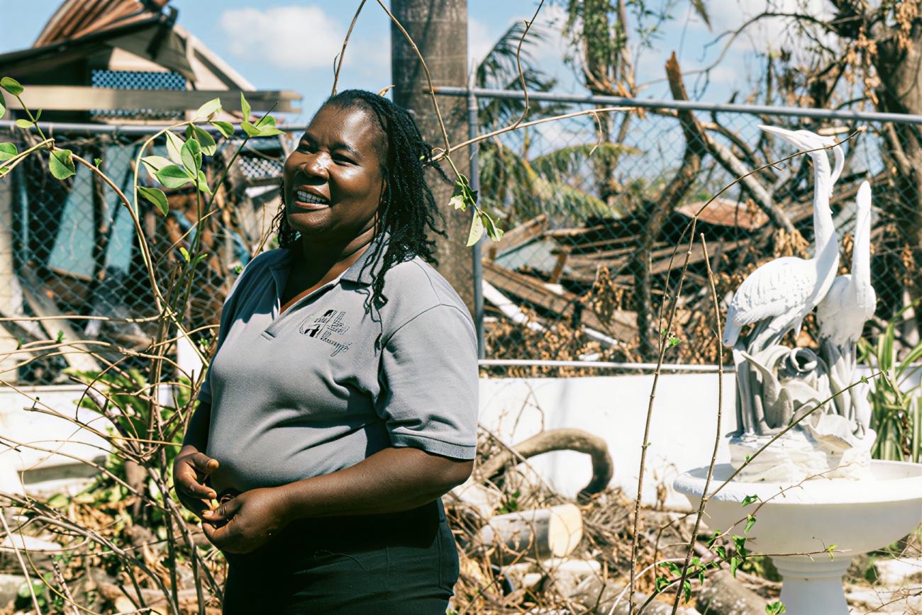 A woman in Jamaica stands in front of destruction brought on by a hurricane.