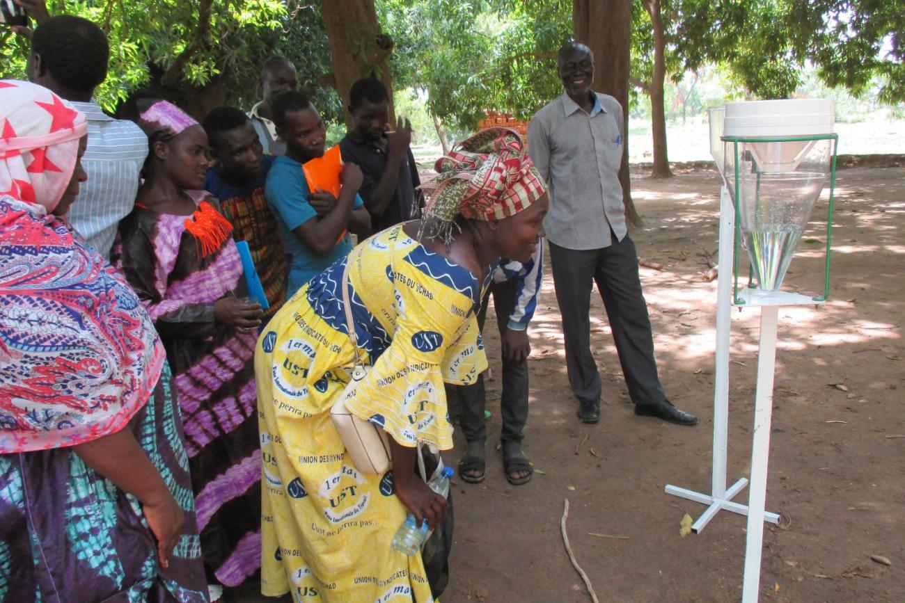 Un groupe de personnes observe une démonstration d’un dispositif de collecte d’eau en milieu rural.