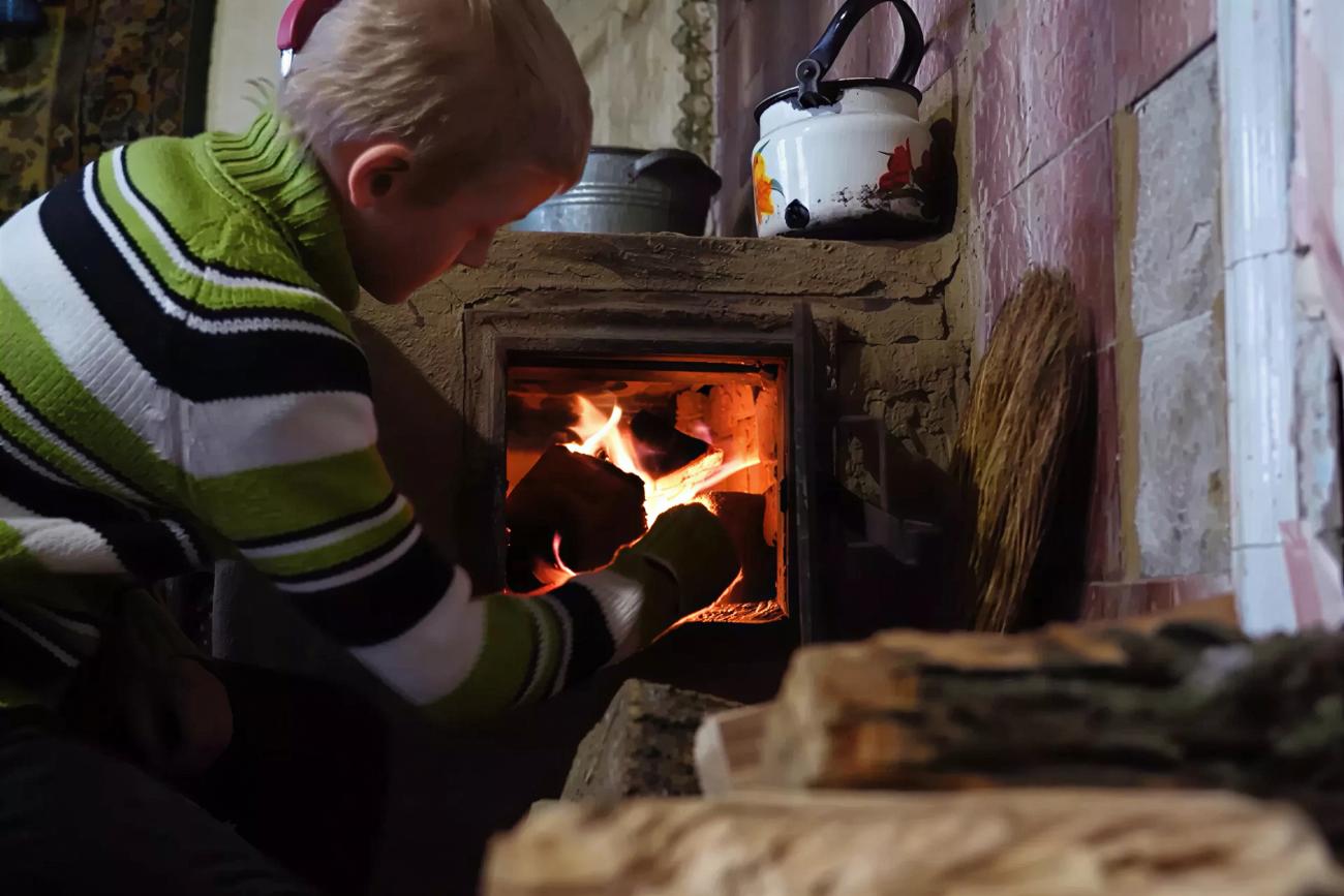 A boy in Ukraine puts firewood in a wood heater.