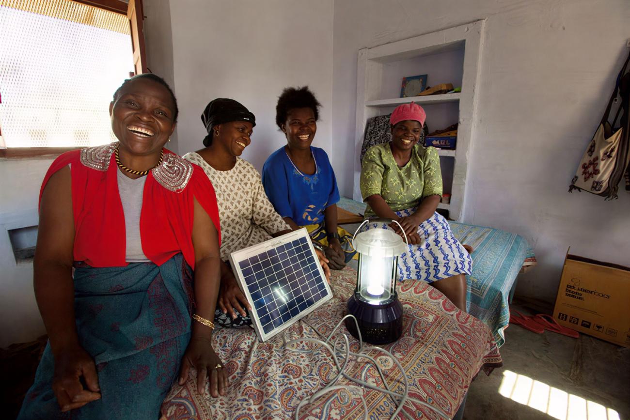 Four women stand around a solar panel.