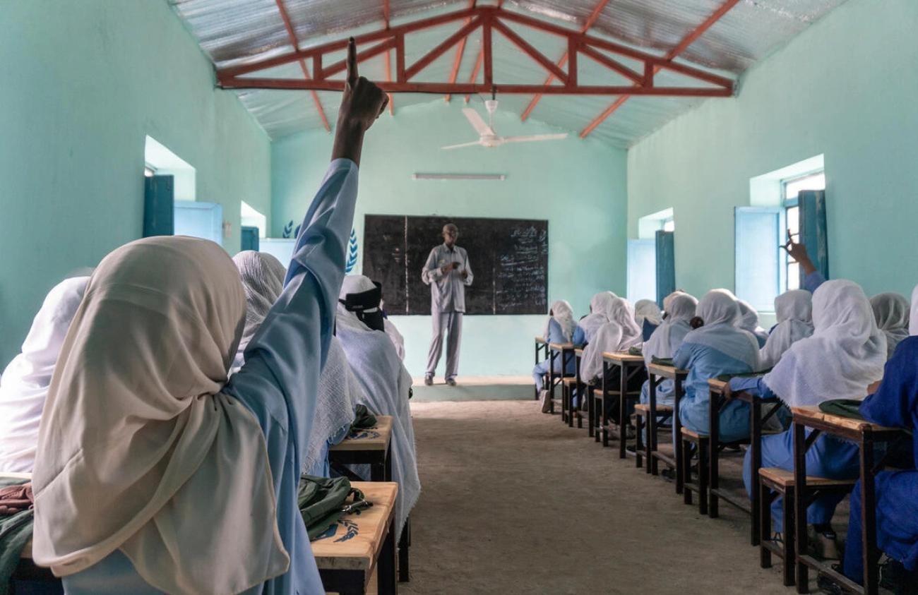 Female students raise their hands in a classroom in Sudan. 