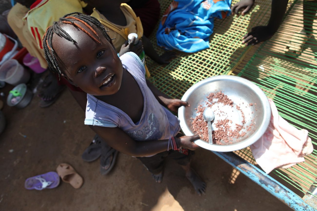 A girl in South Sudan holds a bowl of food.