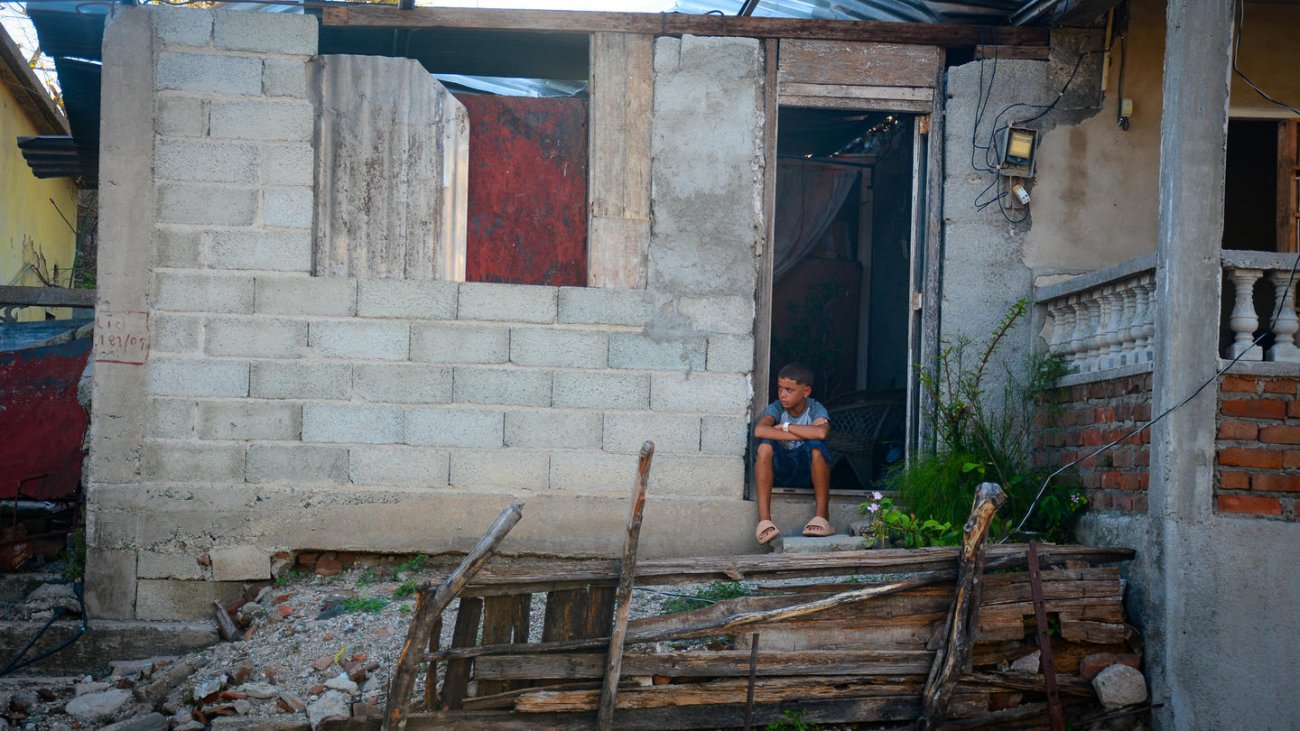 Un niño está sentado frente a su casa en Cuba.