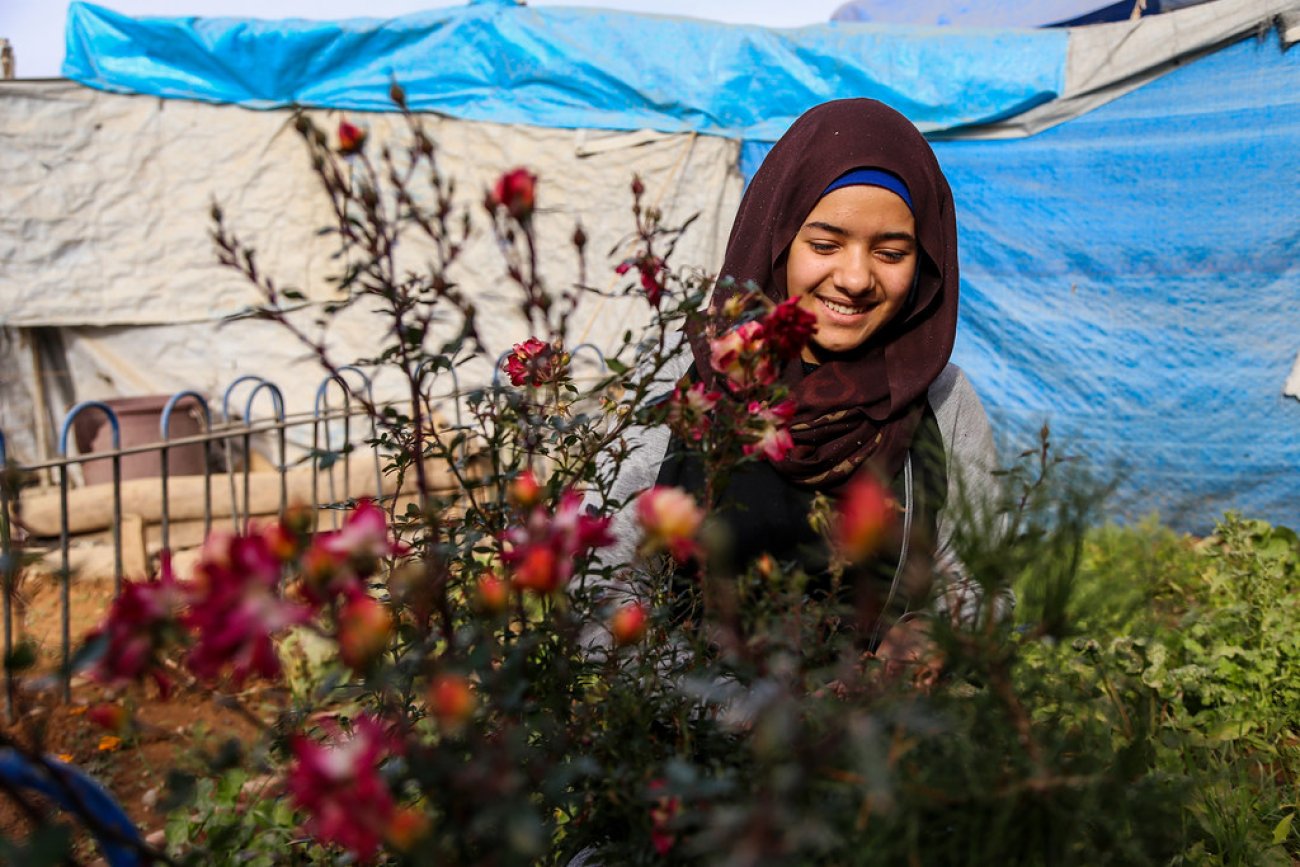 A young woman in Iraq stands in front a small plant.