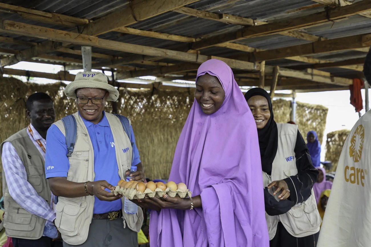 A woman in Nigeria holds a carton of eggs, surrounded by aid workers and local community members.