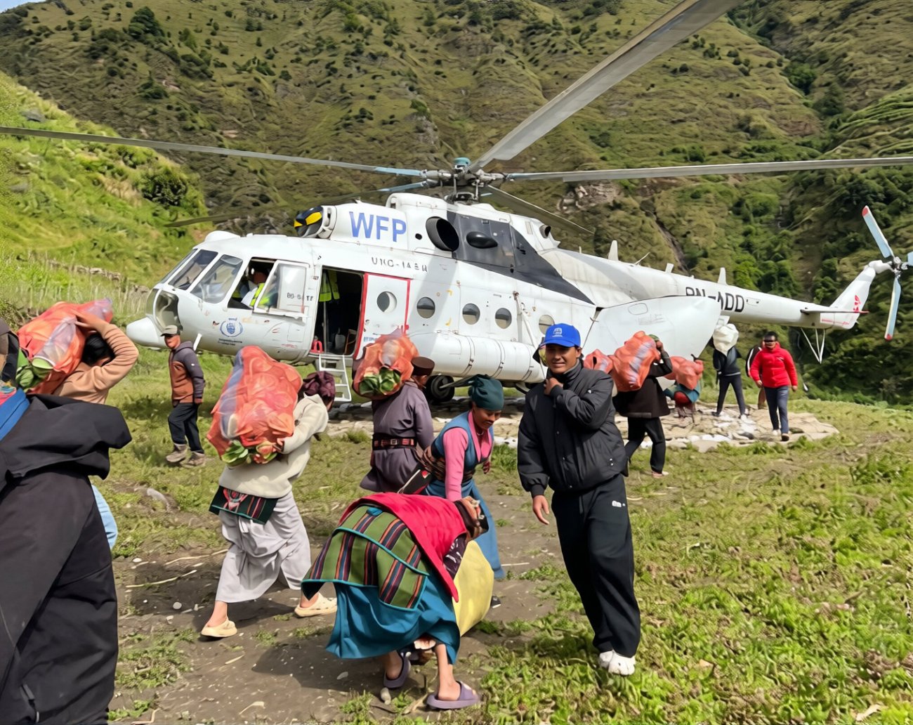 People carry bags of food in Nepal in front of a helicopter.
