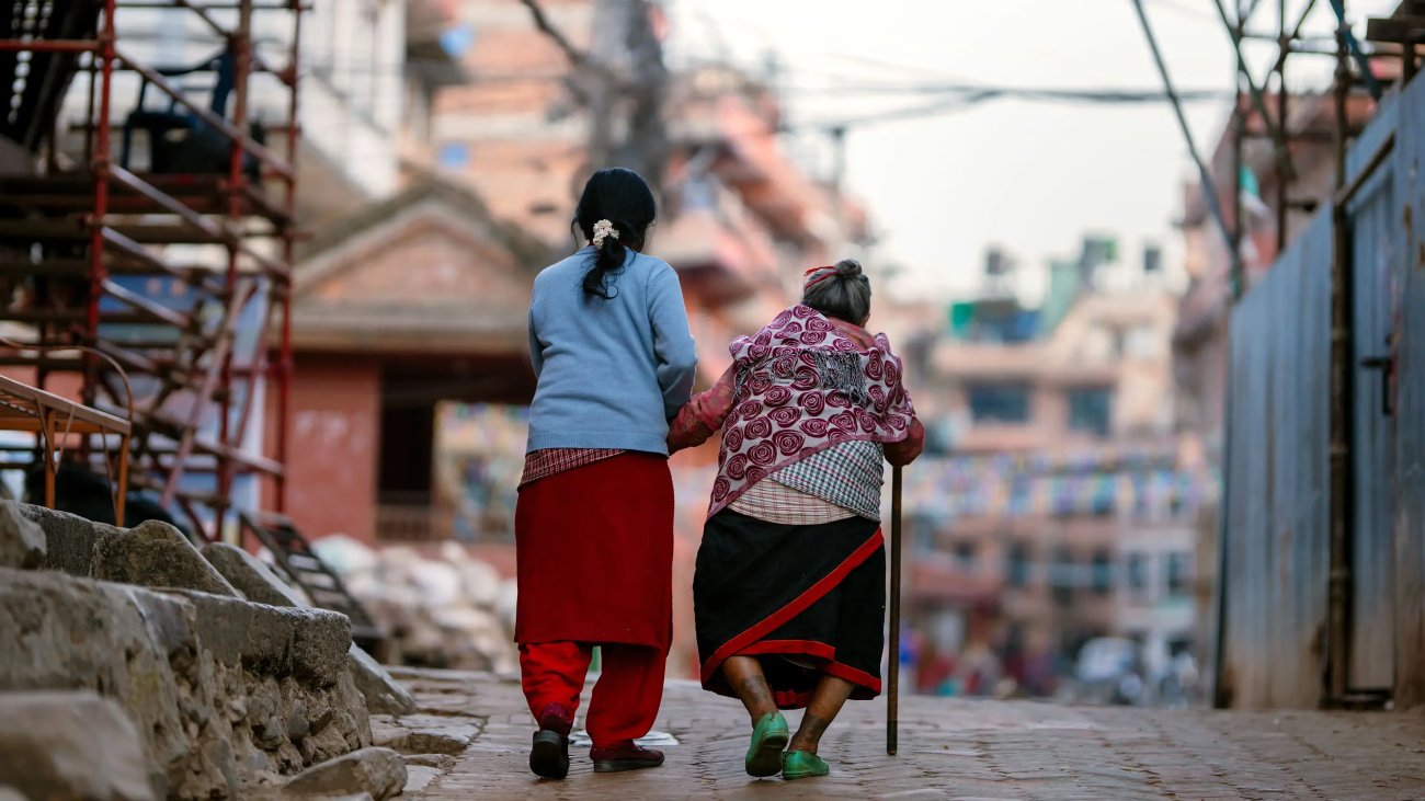 An elderly woman and younger woman in Nepal walk together.