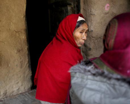 Une femme couverte d’une large voile rouge est assise à même le sol, l’air triste, et discute avec une autre femme, voilée également, assise dos à la caméra.