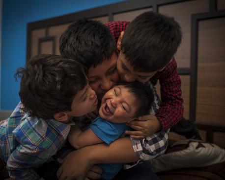 La imagen muestra a tres hermanos abrazando y besando a su hermanito pequeño.